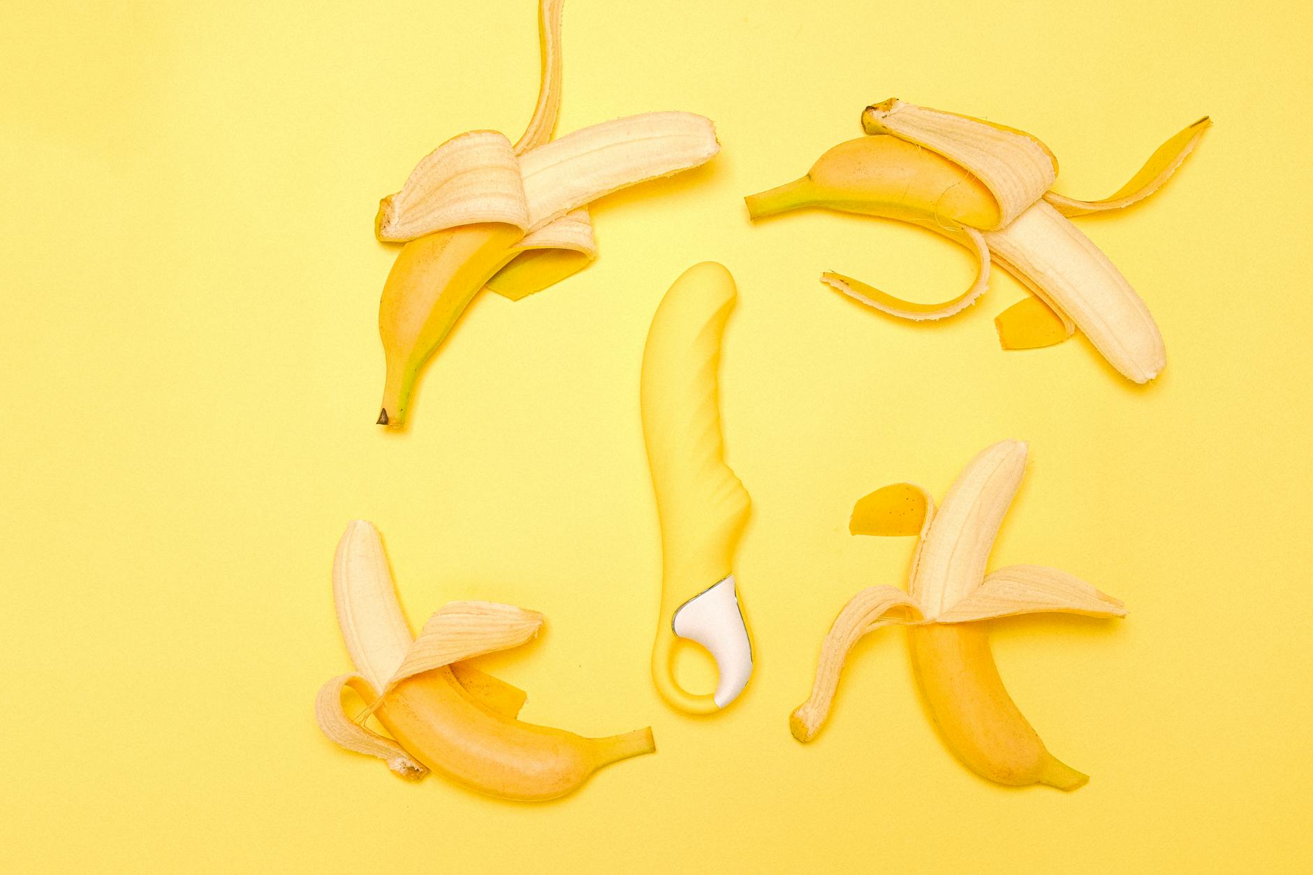 Gelber Silikon-Vibrator, umgeben von geschälten Bananen auf gelbem Hintergrund
