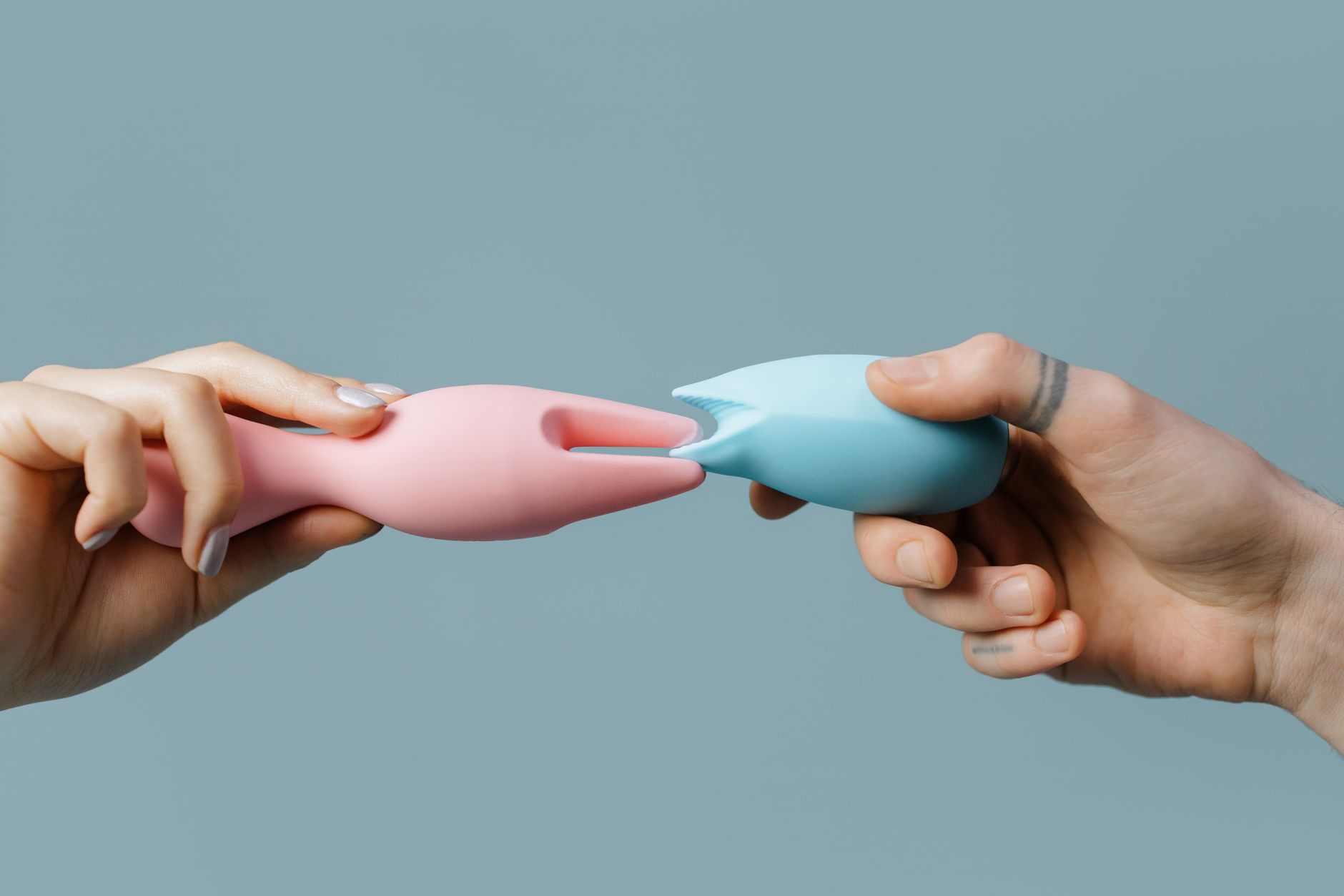 Nahaufnahme einer Hand, die einen orangefarbenen Vibrator gegen einen minimalistischen violetten Hintergrund hält.