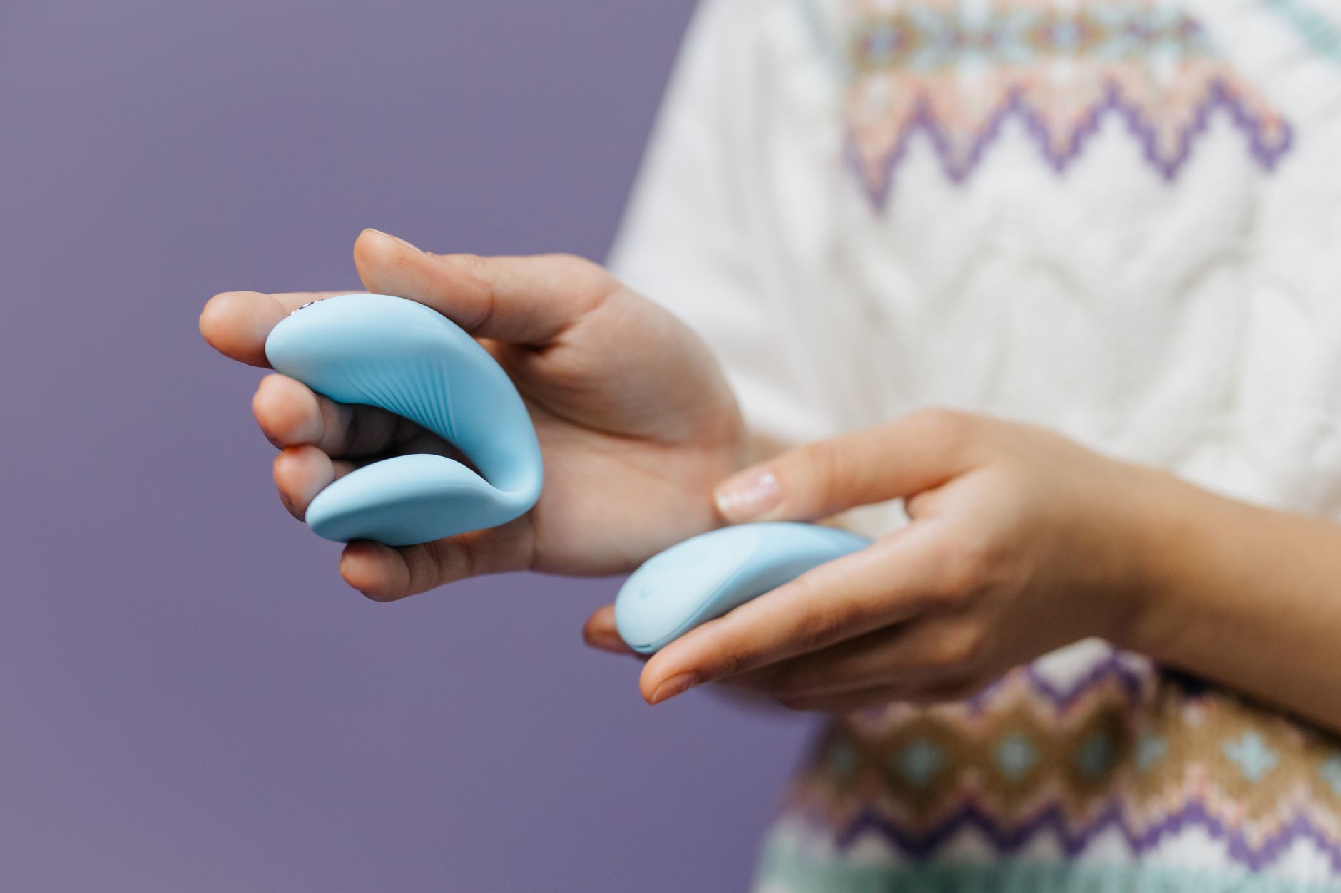 Nahaufnahme: Hände halten einen eleganten blauen Vibrator vor purpurnem Hintergrund