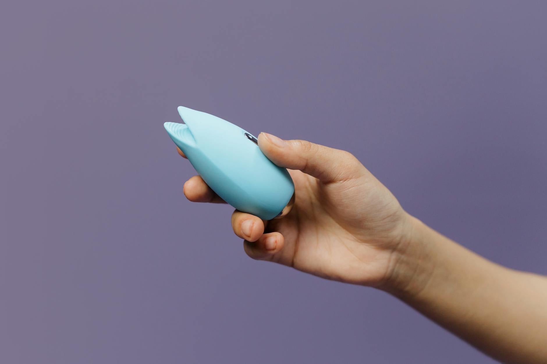 Ein blauer Silikon-Vibrator in einer Hand vor solidem violettem Hintergrund, das Selbstvergnügen und sexuelle Selbstliebe fördernd.