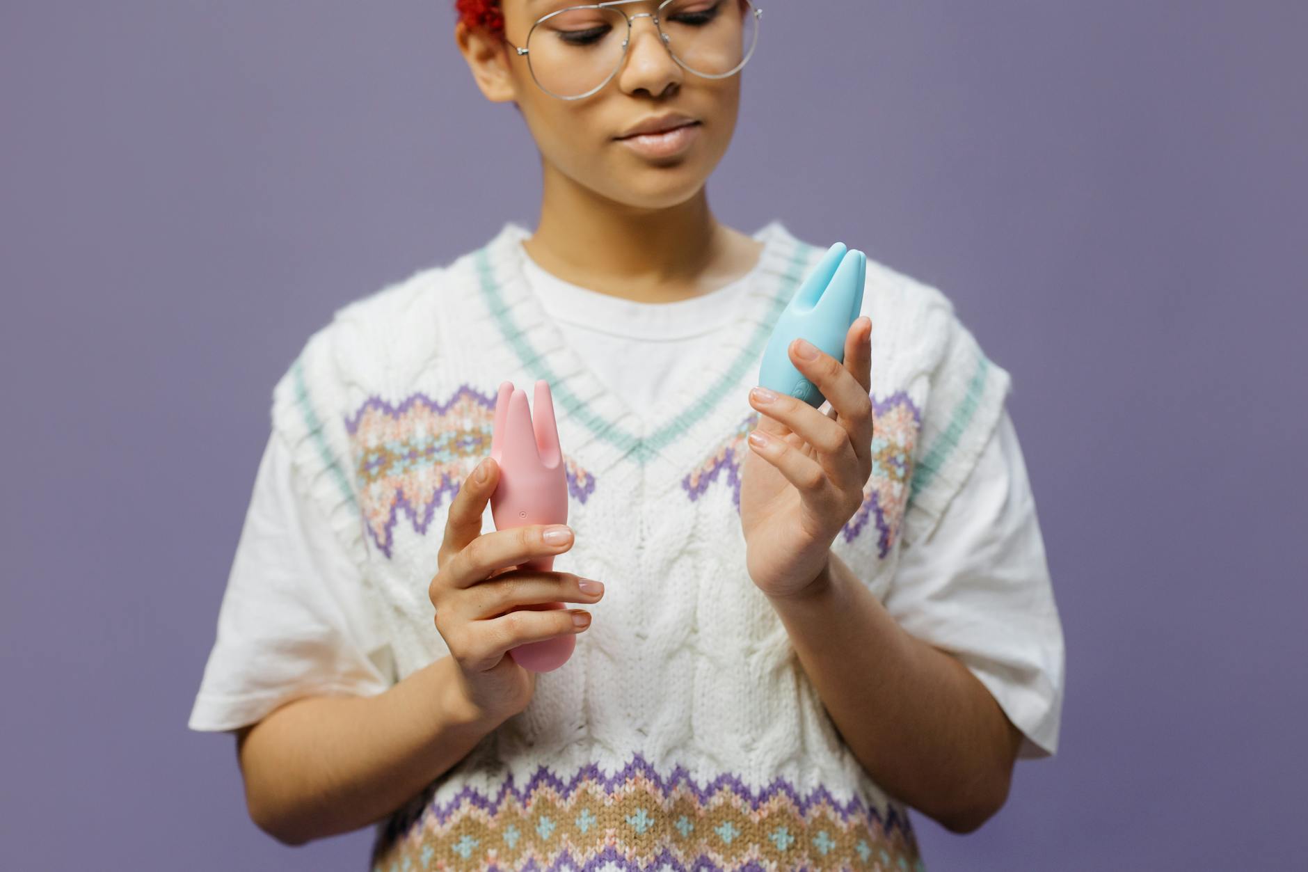 Frau mit Brille hält blaue und rosa Silikonvibratoren in nachdenklicher Weise.
