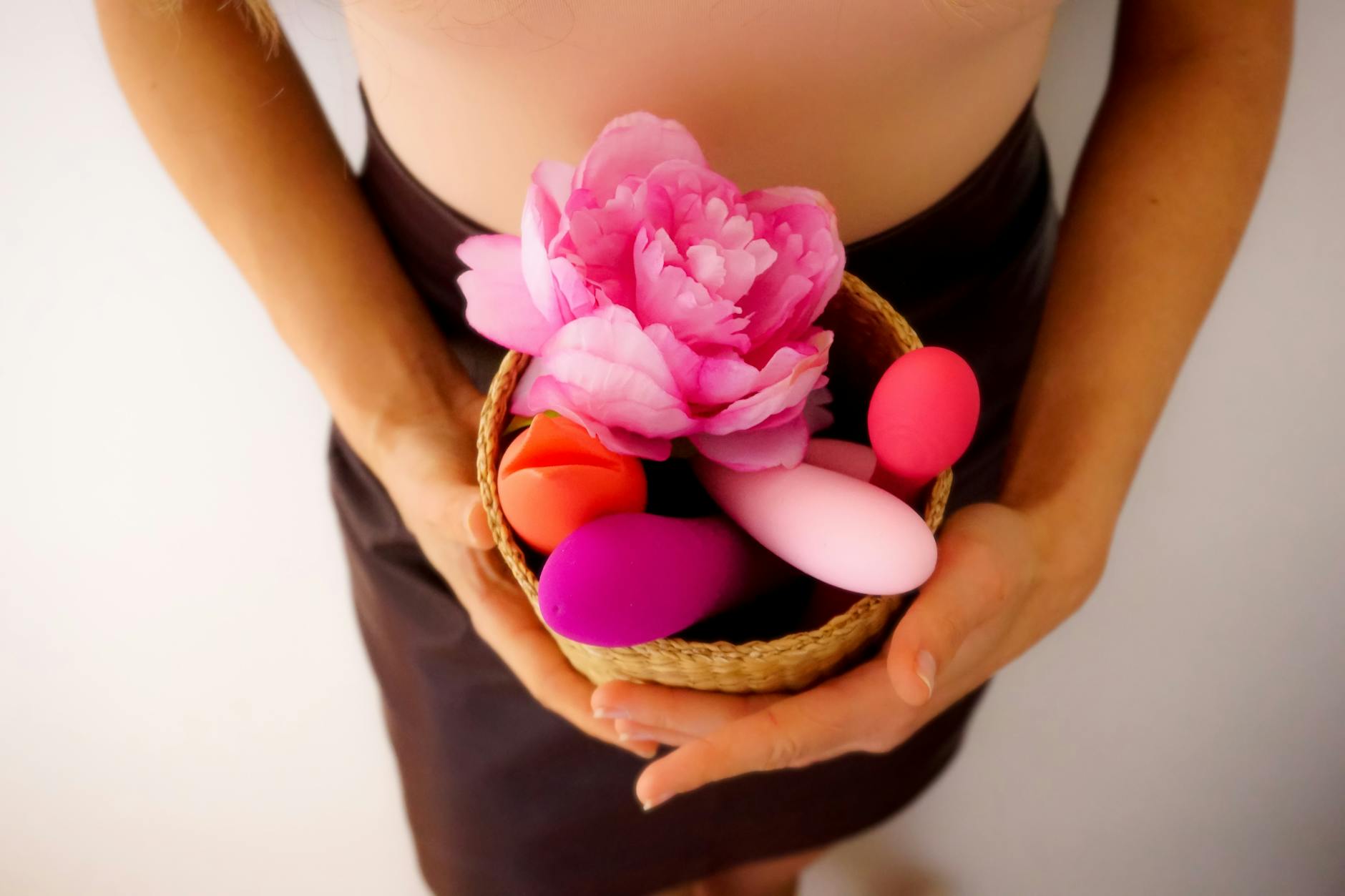 Ein Korb mit bunten Vibratoren und einer rosa Blume, die zeigt, dass Vergnügen viele Formen hat